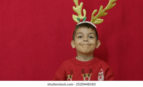 Christmas holidays. Cute boy child adjusting deer antlers isolated on red background. High quality photo - Powered by Shutterstock