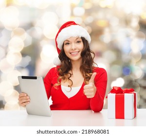 christmas, holidays, technology, gesture and people concept - smiling woman in santa helper hat with gift box and tablet pc computer showing thumbs up over lights background - Powered by Shutterstock