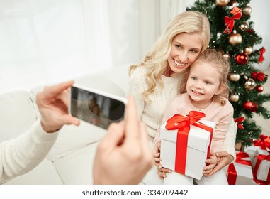 Christmas, Holidays, Technology And People Concept - Happy Family Sitting On Sofa And Taking Picture With Smartphone At Home
