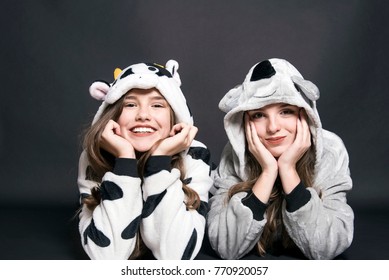 Christmas Holidays. Two Children, Sisters Are Wearing Animal Pajamas. Merry Christmas Or Halloween Concept. Family Holiday, Party Over Black Background. Cute Teenage Sisters. Children Are Lying
