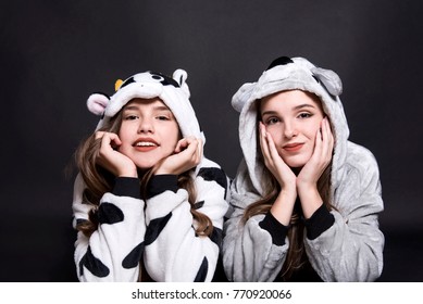 Christmas Holidays. Two Children, Sisters Are Wearing Animal Pajamas. Merry Christmas Or Halloween Concept. Family Holiday, Party Over Black Background. Cute Teenage Sisters. Children Are Lying.
