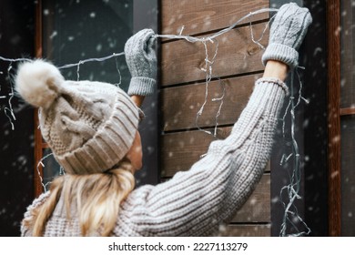 christmas home decorations. woman install electric string lights on house exterior facade - Powered by Shutterstock