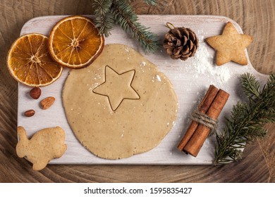Christmas homemade baking background: ginger dough rolled out on a wooden board, cookies, cinnamon and slices of dried oranges. Top view, flat lay