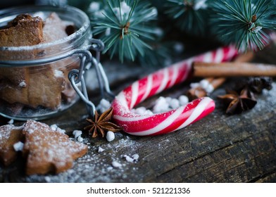 Christmas homemade gingerbread cookies and red candy cane on old wooden table with fir tree. Christmas treats concept. Christmas moody style background. Selective focus. Copy space. Toned image.