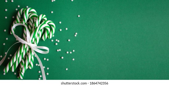 Christmas Horizontal Background With Candy Canes. Green Sweet Sticks With White Ribbon. Flat Lay, Overhead View, Copy Space. Poster, Banner, Greeting Card Template. Festive Backdrop. Holiday Season