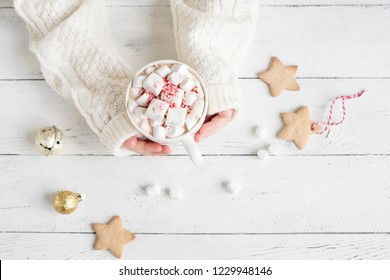 Christmas Hot chocolate with marshmallows, peppermint candies in hands on white table, top view, copy space. Hot cocoa drink for Christmas and winter holidays with festive decor.