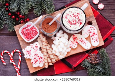 Christmas hot chocolate tray an assortment of sweet toppings. Top view table scene on a dark wood background.