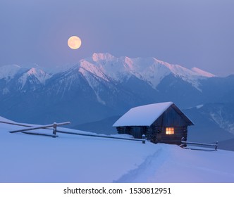 Christmas Landscape With A Snowy House In The Mountains. Fairy Night View With Full Moon. Winter Wonderland With Footsteps In Snow