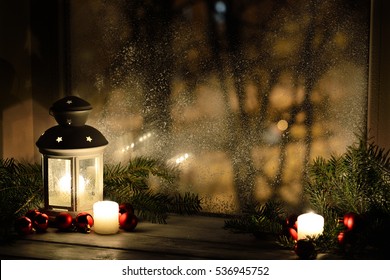 Christmas lantern with snowfall, candles, view from the window on the night street. Background lights