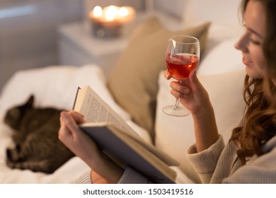 Christmas, Leisure And Comfort Concept - Happy Young Woman Reading Book And Drinking Rose Wine In Bed At Home Bedroom