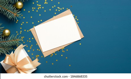 Christmas letter envelope with blank paper card, white gift box with golden ribbon bow, fir branches decorated balls on dark blue background. Flat lay, top view. Letter to Santa Claus concept. - Powered by Shutterstock