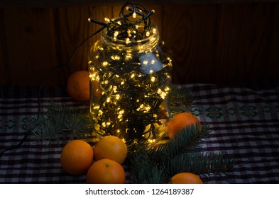 Christmas lights. Decorative lights. Christmas Eve. Warm white led lights. Christmas light decorations in a jar, tangerines and spruce branches on a checkered tablecloth in the dark. - Powered by Shutterstock