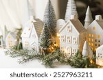 Christmas little ceramic houses, snowy trees and golden lights on dark background in eve. Merry Christmas! Atmospheric Christmas scene, miniature holiday village. Xmas background