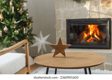 Christmas modern decoration on table against burning fireplace. Stylish wooden star decor in festive room, christmas eve time. Atmospheric christmas time.