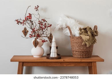 Christmas mood. A Christmas bouquet with paper toys, a ceramic Christmas tree, a basket with cozy blankets on a wooden oak bench in the living room   
