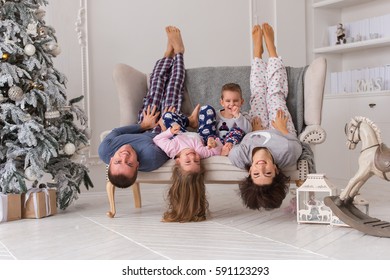 Christmas morning. Beautiful family (mom, dad, son and daughter) in sleepwear lying on a sofa upside down.