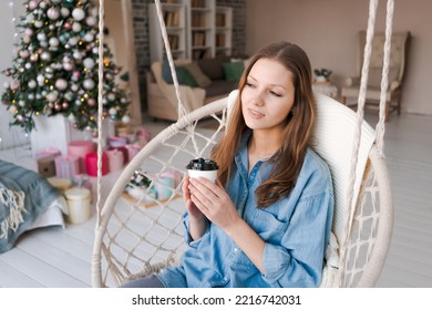 Christmas Morning, Christmas. Girl On Chair Drinks From Disposable Paper Cup. Woman On New Year's Eve In Rustic Retro Living Room. Enjoying Winter Holidays