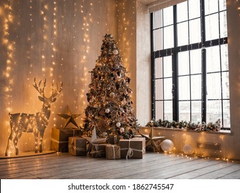 Christmas morning interior with christmas tree decorated deer and big window. Beige cozy loft with lights. Vintage interior. Gold balls on the Christmas tree. Xmas gifts in craft paper. New Year.
