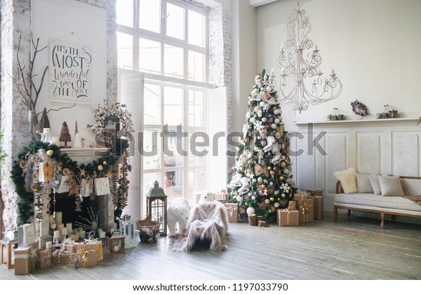 クリスマスの朝のインテリアとクリスマスツリーの飾り付けされた暖炉と大きな窓 白いロフト ビンテージシャンデリア ベージュのソファ クリスマスツリーの上に白と金のボール 北極熊 新年 の写真素材 今すぐ編集