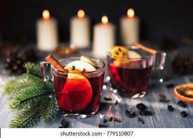 Christmas mulled wine on wooden background. Hot alcohol drink with sliced oranges and apple. Fir-tree branches, cinamon, cloves, candles