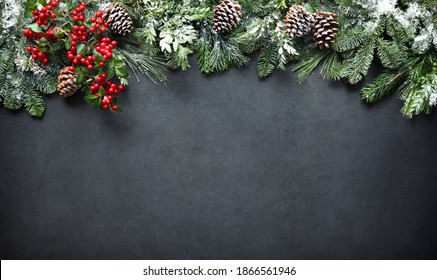 Christmas and New Year background with fir branches, holly and snowfall on dark stony board - Powered by Shutterstock