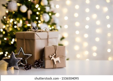 christmas and new year background - gift boxes and stars near decorated christmas tree and copy space over white wall with garland lights