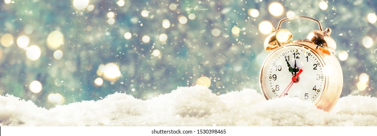 Christmas Or New Year Background With Golden Alarm Clock In Snowdrifts On Blue Background With Holiday Lights Counting Last Moments Before Christmass Countdown To Midnight. 