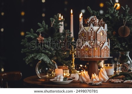 Christmas and New Year beautiful elegant family dinner table setting decorated with candles, fir tree branches, handmade craft toys. Gorgeous big homemade cake with gingerbread houses as centrepiece