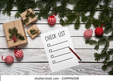 Christmas, New Year Check List. Paper Sheet With A List On White Planks Edged By Green Fir Branches With Gift Boxes