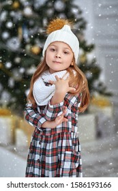 Christmas and New Year concept. Pretty little girl in warm clothes posing near the beautiful Christmas tree. Winter kid's fashion.