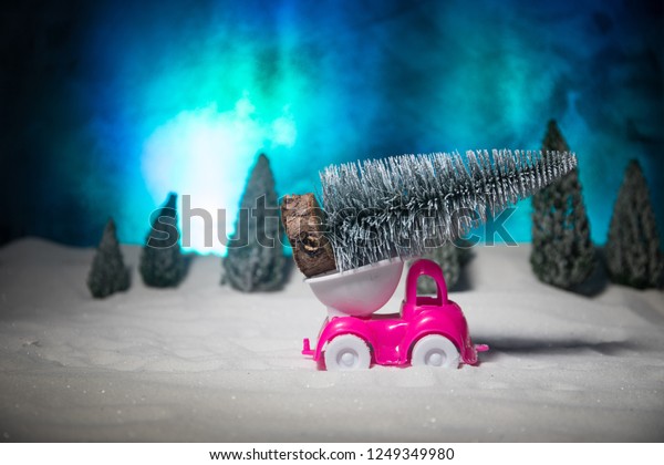 Christmas or New Year concept. Toy car carrying a\
Christmas tree through the forest in snowfall. Holiday decorated\
background. Selective\
focus