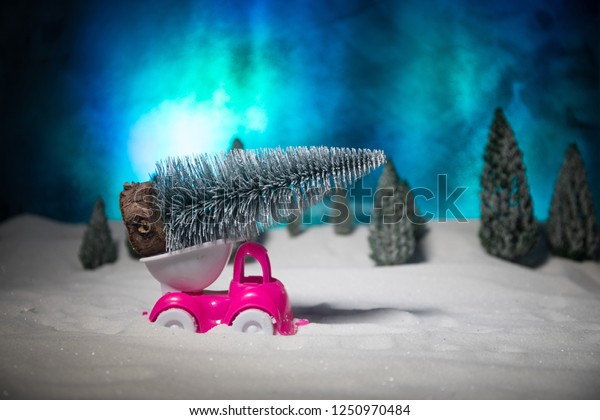 Christmas or New Year concept. Toy car carrying a\
Christmas tree through the forest in snowfall. Holiday decorated\
background. Selective\
focus