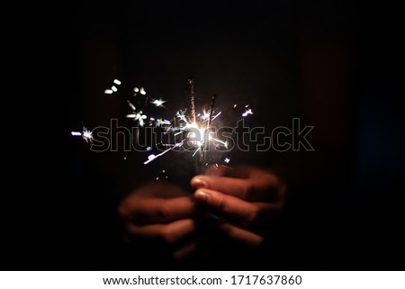 Christmas and new year eve concept image with close up of a pair of man hands taking a red fire sparkler to celebrate the night party - focus on fireworks and hope for people future