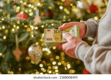Christmas and New Year expenses.pack of euro money in hands on a Christmas trees background.Spending on gifts and Christmas decor.Expenses during the winter holidays