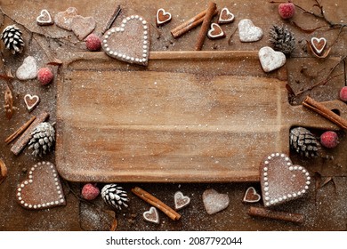 Christmas or New Year greeting card in brown tones. Wooden board on a table with gingerbread hearts, cinnamon sticks, pine cones, red apples covered with snow like sugar powder. Space for text - Powered by Shutterstock