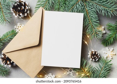 Christmas or New Year greeting card mockup with envelope, fir tree branches with cones and lighting garlands - Powered by Shutterstock