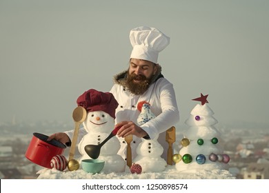 Christmas And New Year Holidays Food. Happy Cook, Snowmen And Snow Xmas Tree On Blue Sky. Cooking And Diet Concept. Hipster With Ladle In White Uniform. Man In Chef Hat Ladling Soup On Winter Day.