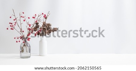 Christmas, New Year home decor. Branches with red berries in a glass vase on a light background. Mock up for displaying works