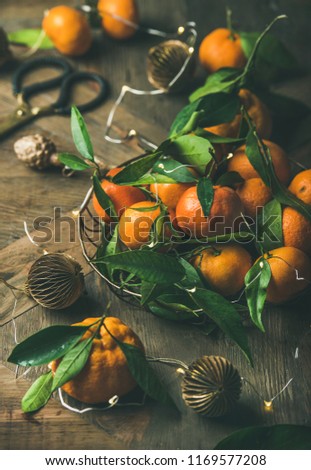 Christmas or New Year table. Fresh ripe tangerines with leaves in tray, decoration toys, scissors and light garland over rustic wooden table background, selective focus, close-up