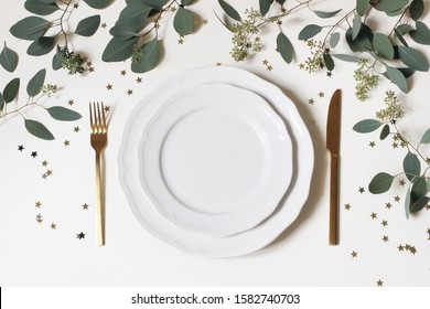 Christmas, New Year Table Place Setting. Golden Cutlery, Porcelain Plate, Eucalyptus Branches And Golden Confetti Stars Isolated On White Background. Winter Holidays Background. Flat Lay, Top View.