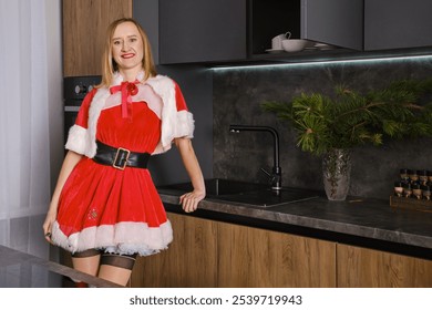 Christmas and New Year theme: smiling woman in Santa costume posing in the kitchen - Powered by Shutterstock