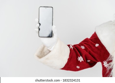 Christmas And New Years Concept. Santa Claus Holds A Mobile Phone In His Hand. No Face Visible. Isolated Background