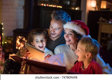 Christmas night, a cheerful family opening their presents  at the foot of the Christmas tree. They find a digital tablet in a gift box