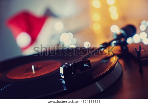 Christmas,
Noel. Turntable vinyl record player. Sound technology for DJ to mix
& play music. Vintage vinyl record player on a background of
Christmas decorations, cap, wreath and lights
