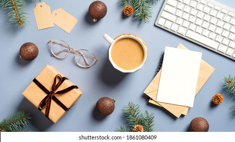 Christmas office table with coffee cup, gift box, computer keyboard, glasses, Xmas decorations, Christmas card on pastel blue background. Flat lay, top view. New Year workspace.