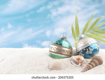 Christmas on the Beach with Two Vintage Ornaments, Sea Shells and palm frond.  White sand and blue sky with clouds as background with room or space for copy, text, words.  Horizontal - Powered by Shutterstock