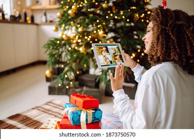 Christmas online holiday. Happy woman having video call with their family or friends. Young woman uses a digital tablet near decorated festive tree at home. Virtual meeting. Covid-2019. - Powered by Shutterstock