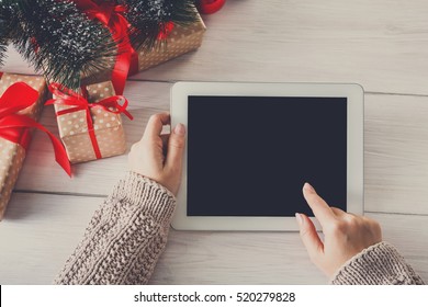 Christmas online shopping above view on wood. Female buyer touch screen of tablet, copy space. Woman has coffee, buys presents near christmas tree, among gift boxes. Winter holidays sales background