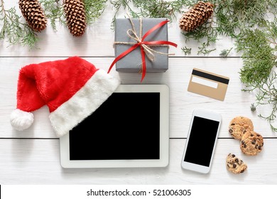 Christmas Online Shopping Background. Mobile And Tablet Screen With Copy Space Top View On White Wood, Credit Card, Present Boxes And Santa Hat. Internet Commerce On Winter Holidays Concept