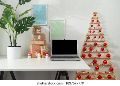 Christmas Online Shopping Concept. Laptop And Gifts On A White Desk, Original Christmas Tree From Branches In A Home Office. Morning Sunshine.